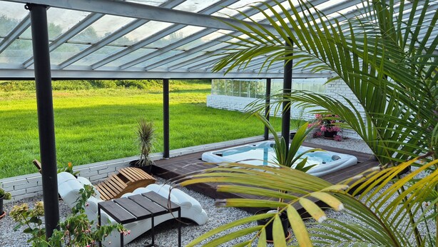 Een overdekt buitengebied met een jacuzzi, zitplaatsen en uitzicht op een grasveld.