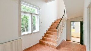 Een trap met een leuning, een raam met uitzicht op groen, en een radiator aan de muur.