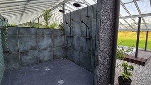Een moderne douche ruimte met donkere tegels en een accentmuur van steen, een glazen broeikasconstructie en uitzicht op een groen landschap.