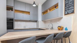 Een moderne keuken met grijze kastjes, een houten aanrecht, een ingebouwde oven en een bar met grijze krukken.