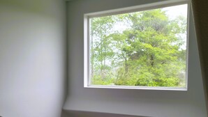 A room with a sloped ceiling, a ceiling fan, and a large window with a view of trees. There are two smaller windows with blinds.