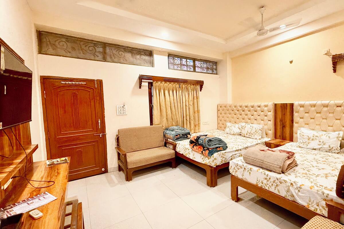 A bedroom with two beds, a television, a chair, and a window with curtains.