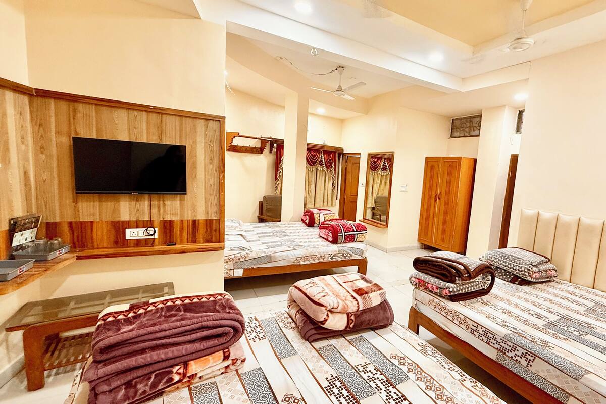 A hotel room with two beds, a flat-screen TV mounted on the wall, a ceiling fan, and a wooden wardrobe.