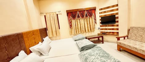 A hotel room with a bed, a sofa, a TV mounted on the wall, and a window with curtains.