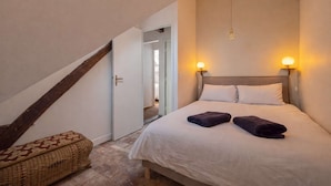 Ein Schlafzimmer mit einem Bett, zwei Wandleuchten, einer hölzernen Bank und einer Tür zu einem anderen Raum.