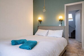 Un lit avec du linge de lit blanc, deux serviettes bleues et deux lampes fixées au mur.