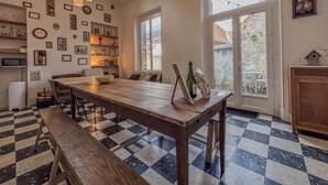 Un comedor con mesa de madera y bancos, suelo de cuadros, luces colgantes y vistas amplias por grandes ventanales.