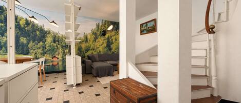 A modern interior with a staircase, a sofa, a wooden chest, and a painting on the wall.
