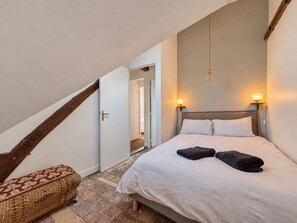 Un dormitorio con cama, mesita de noche, lámpara colgante y una puerta que da a otra habitación.