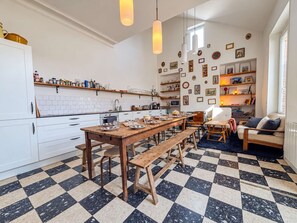 Una cocina con suelo de cuadros, mesa de madera y bancos, con un comedor y un sofá al fondo.