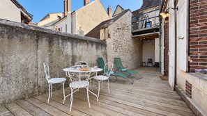 Una terraza de madera con una mesa y sillas, un muro de piedra y un edificio de ladrillo.