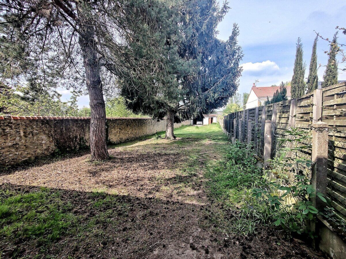 Ein Garten mit einem großen Baum, einer Steinmauer und einem Holzzaun.