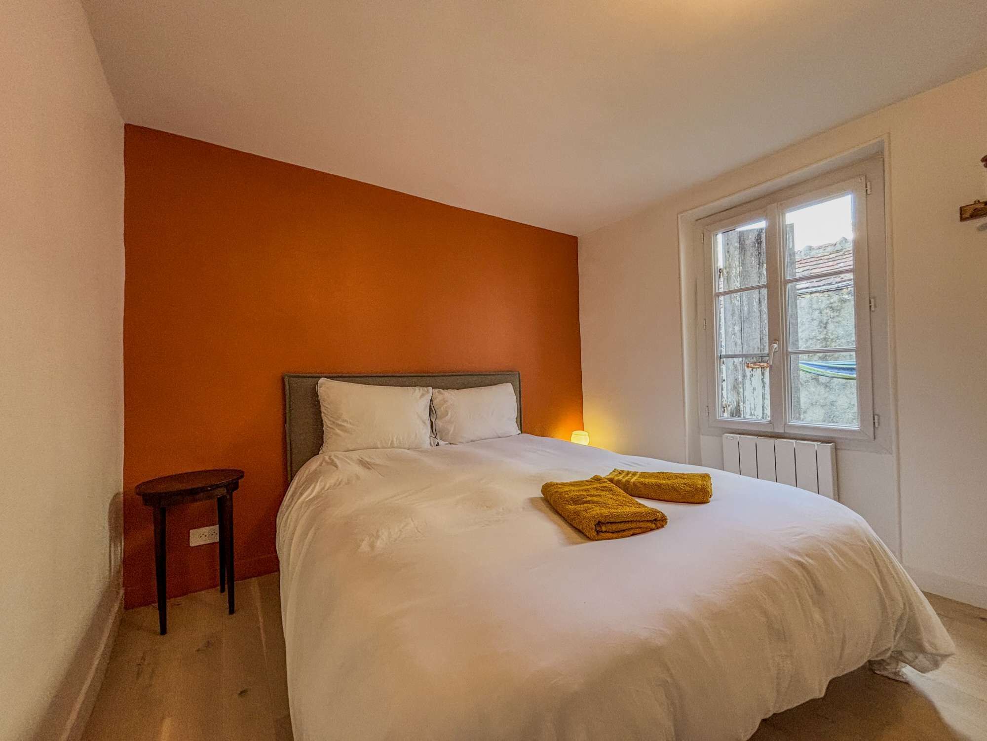 Une chambre à coucher avec un lit, une petite table de chevet et une fenêtre.