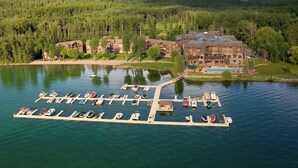 A lakeside lodge with a dock and boats, surrounded by forest and mountains. - Live the Lodge Life | Luxe Home Near Trails, Lake & Spa Amenities (Whitefish)