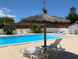 Ein Swimmingpool mit Liegestühlen und einem Strohdachschirm.
