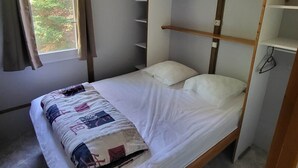 A single bed with a wooden frame and a headboard, a window with curtains, and a wall-mounted shelf.