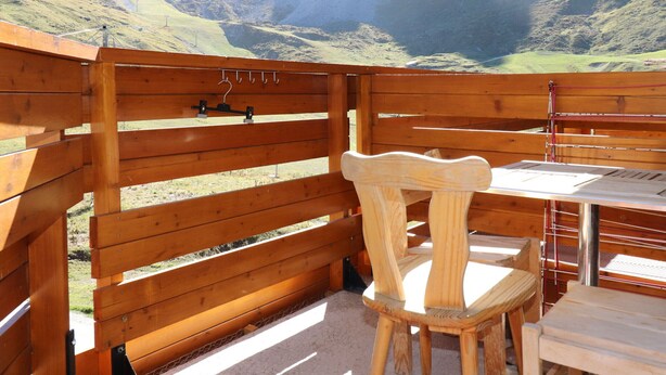 Une terrasse en bois avec une table et des chaises, offrant une vue sur un paysage montagneux.