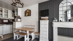 Une cuisine de taille réduite avec des meubles blancs, une table à manger en bois et un téléviseur fixé au mur au-dessus de la table.