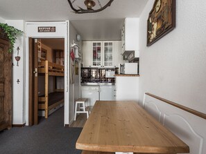 Eine kompakte Küche mit weißen Schränken, einem Holztisch und einem Etagenbett im Hintergrund.