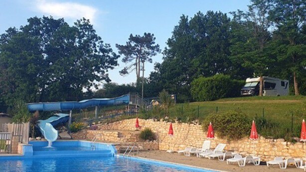 Une piscine avec un toboggan, des chaises longues et un mur en pierre.