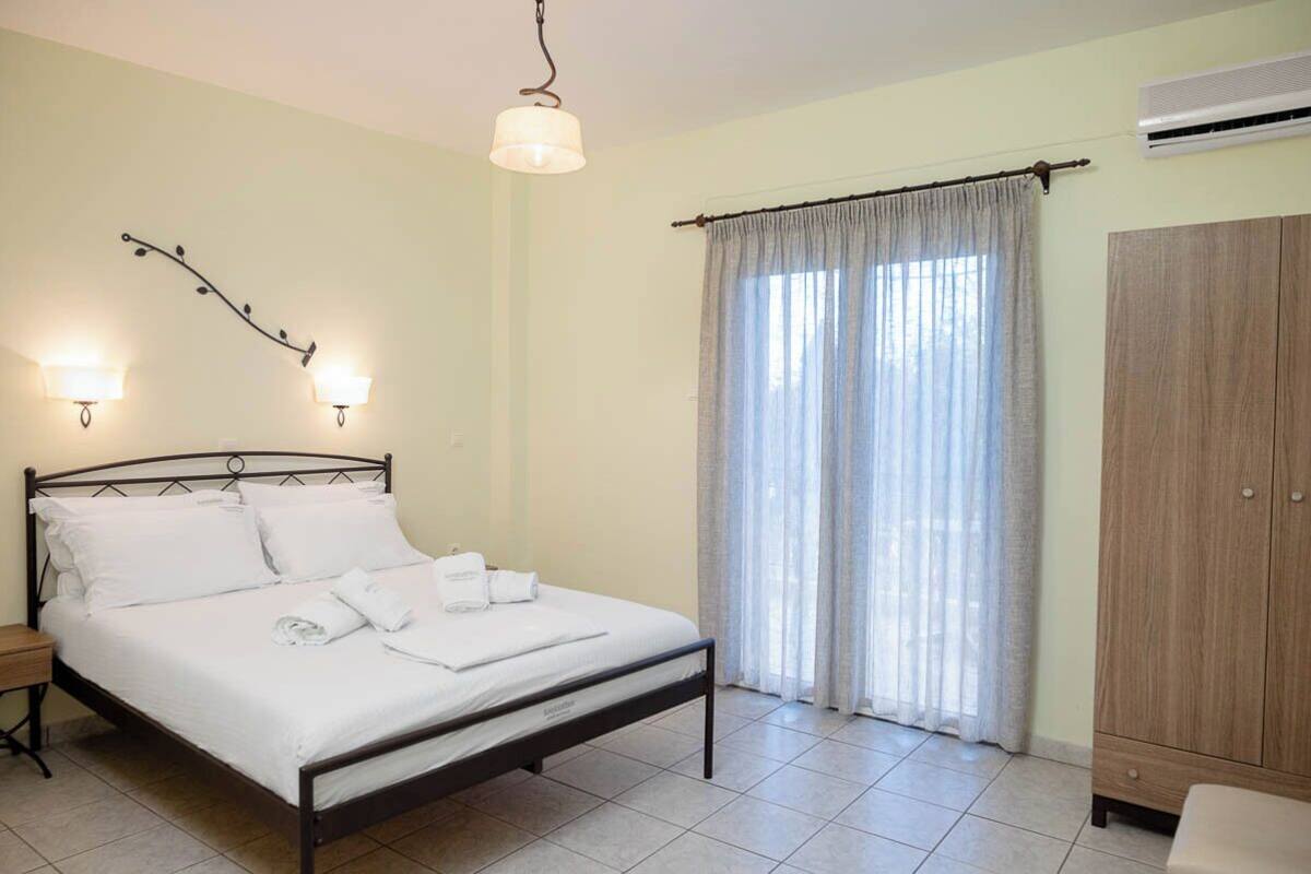 A neatly made bed with white linens, a wooden wardrobe, and a window with sheer curtains.