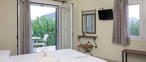 A hotel room with a bed, a TV mounted on the wall, a balcony with a chair, and a window with curtains.