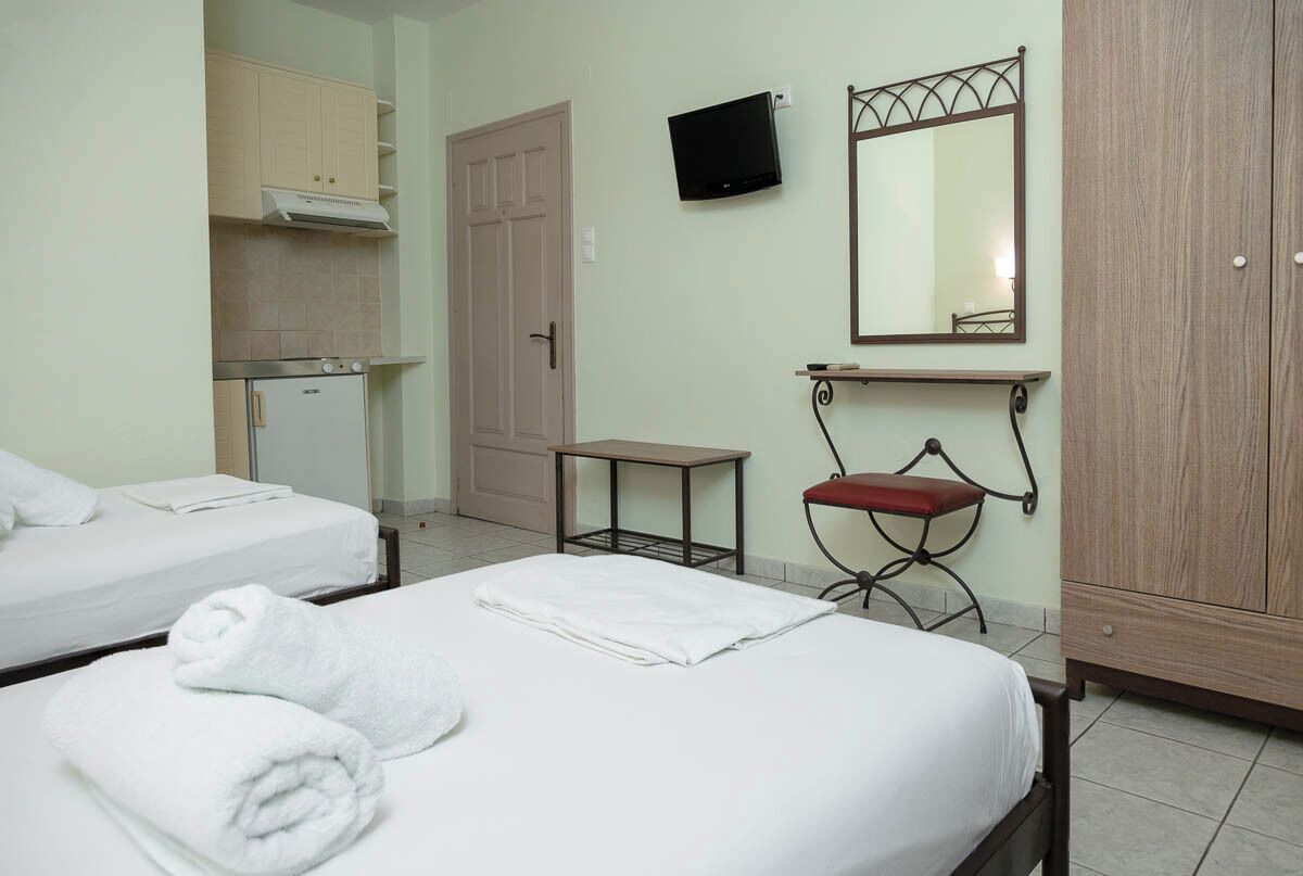 A hotel room with two beds, a small kitchenette, a TV, a mirror, and a wardrobe.