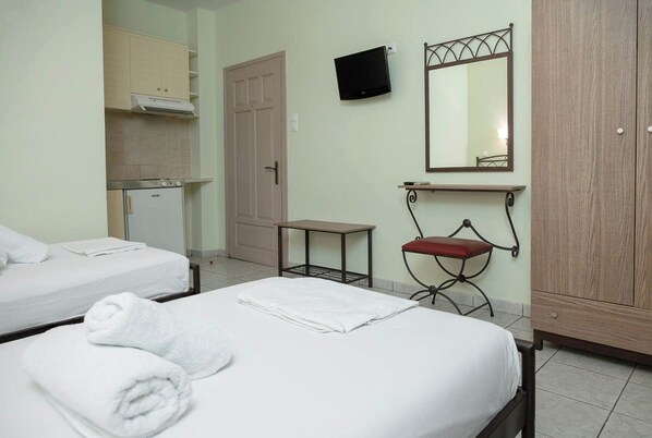 Habitación de hotel con dos camas, una kitchenette pequeña, televisor, espejo y armario.
