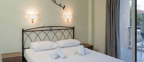 A neatly made bed with white linens and rolled towels, two wall-mounted lamps, and a balcony with a curtain.