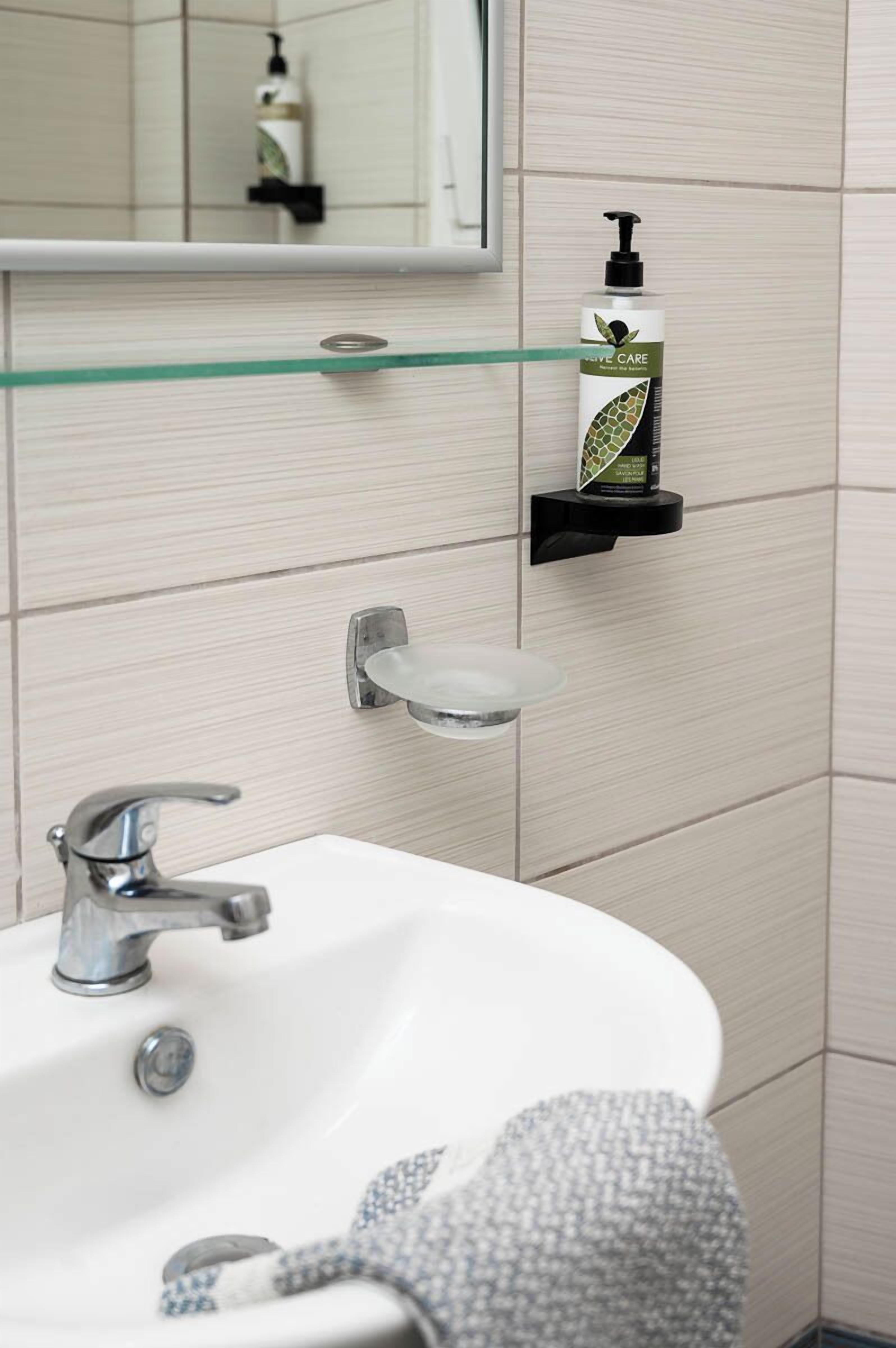 A bathroom with a white sink, a glass shelf with a soap dispenser, and a mirror above the sink.