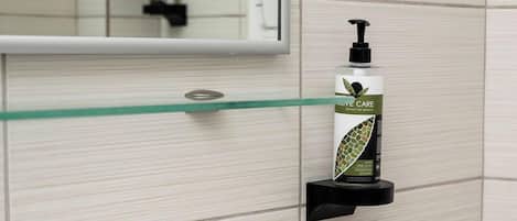 A bathroom with a white sink, a glass shelf with a soap dispenser, and a mirror above the sink.
