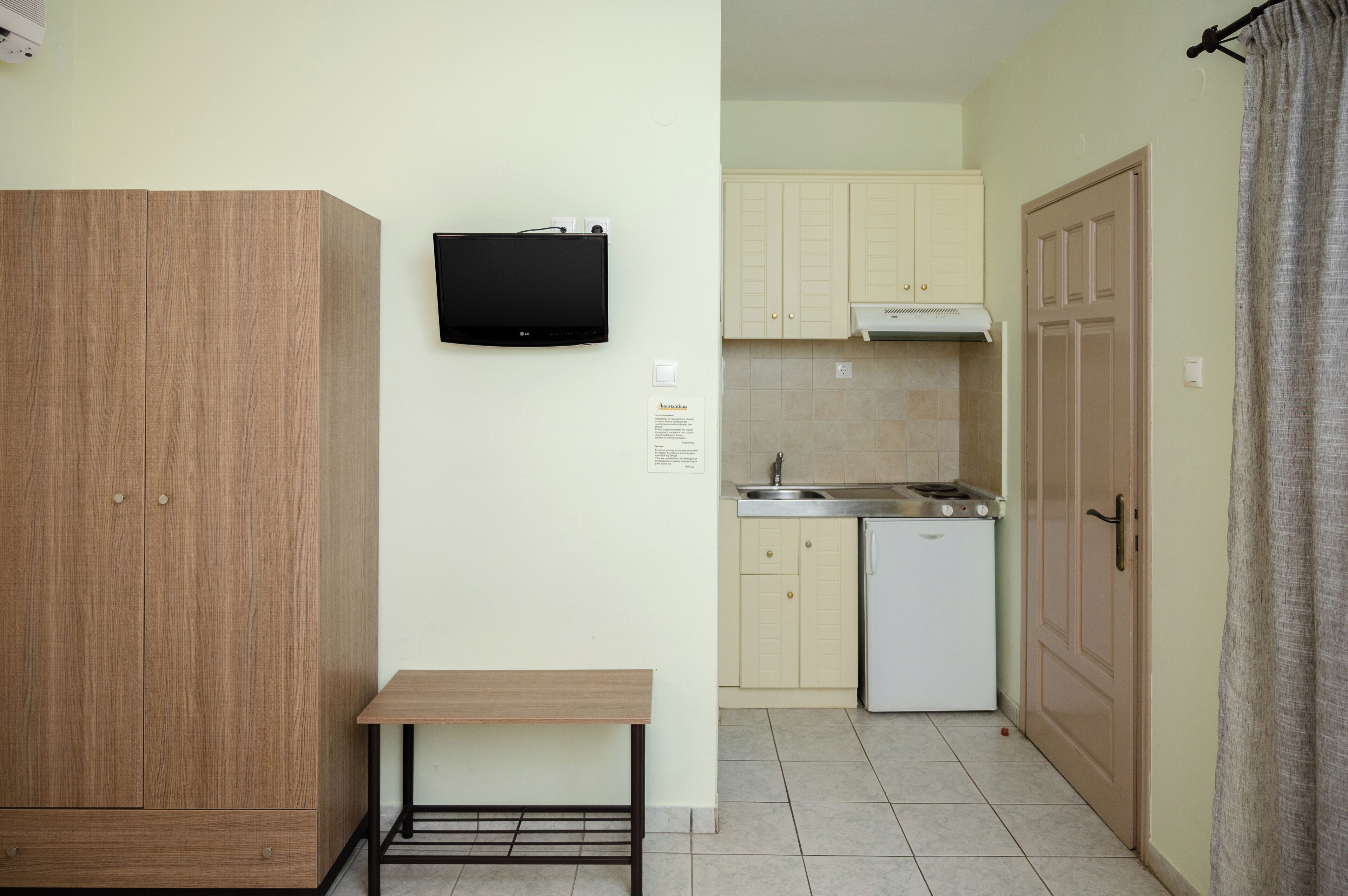 A compact kitchen with a built-in dishwasher, a small table, and a TV mounted on the wall.