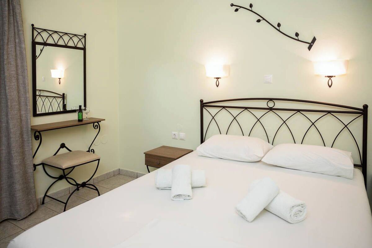 A hotel room with a bed, a bedside table, a chair, a mirror, and wall sconces.