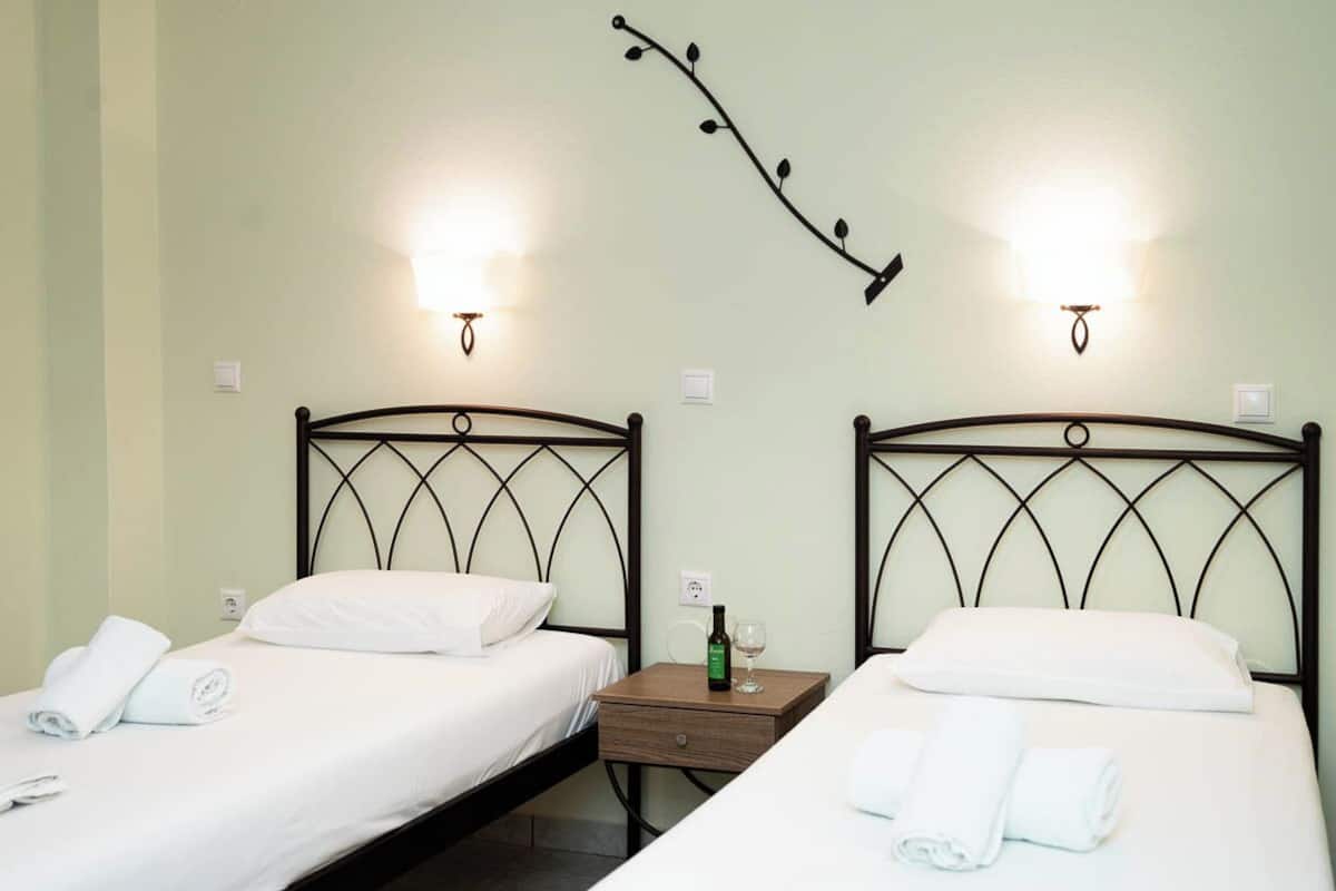Two single beds with metal headboards, white linens, and a nightstand with a bottle and glass.