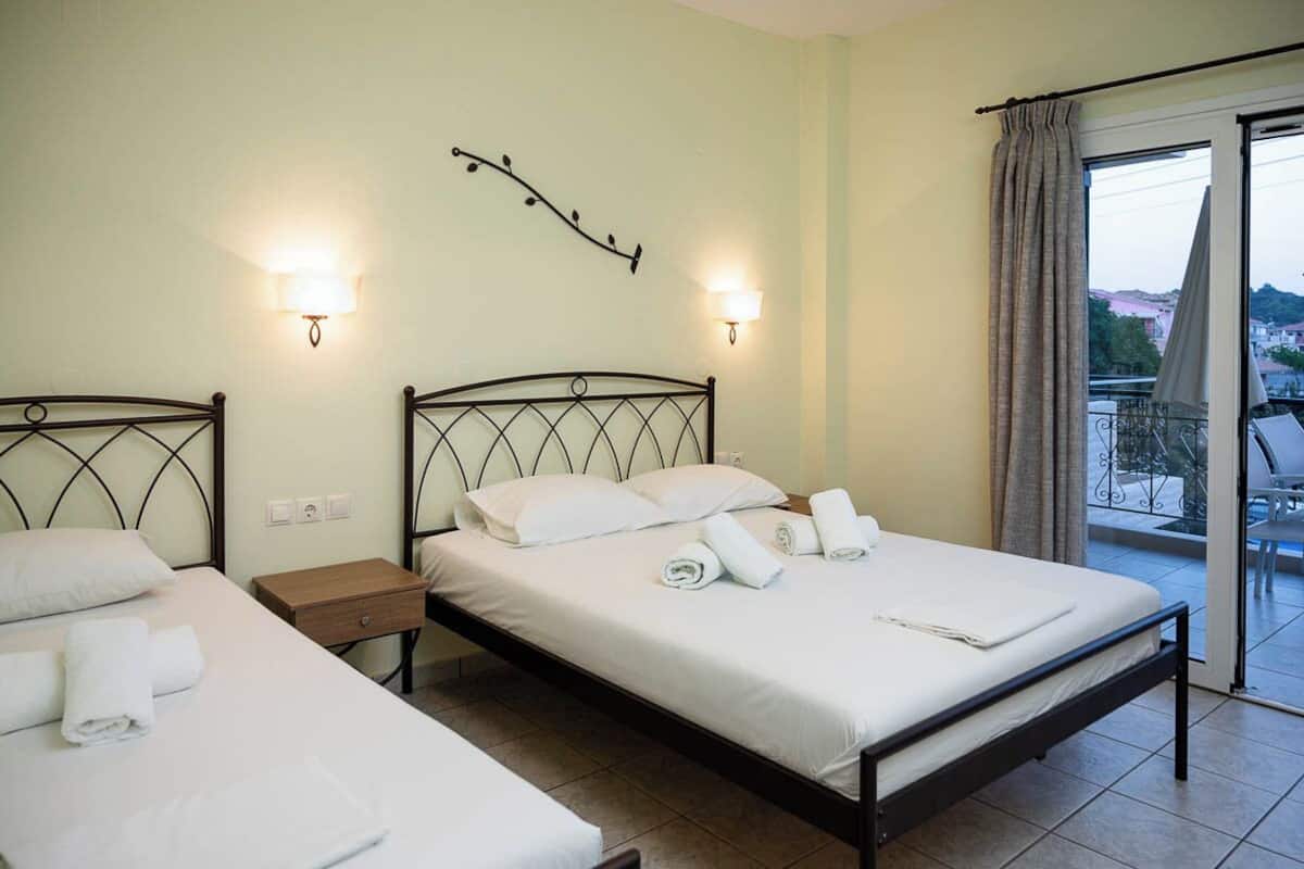 A hotel room with two beds, a balcony with a view, and wall-mounted lights.