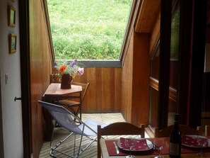 Un comedor con una mesa dispuesta para dos personas, una ventana con vistas a la vegetación y una botella de vino sobre la mesa.
