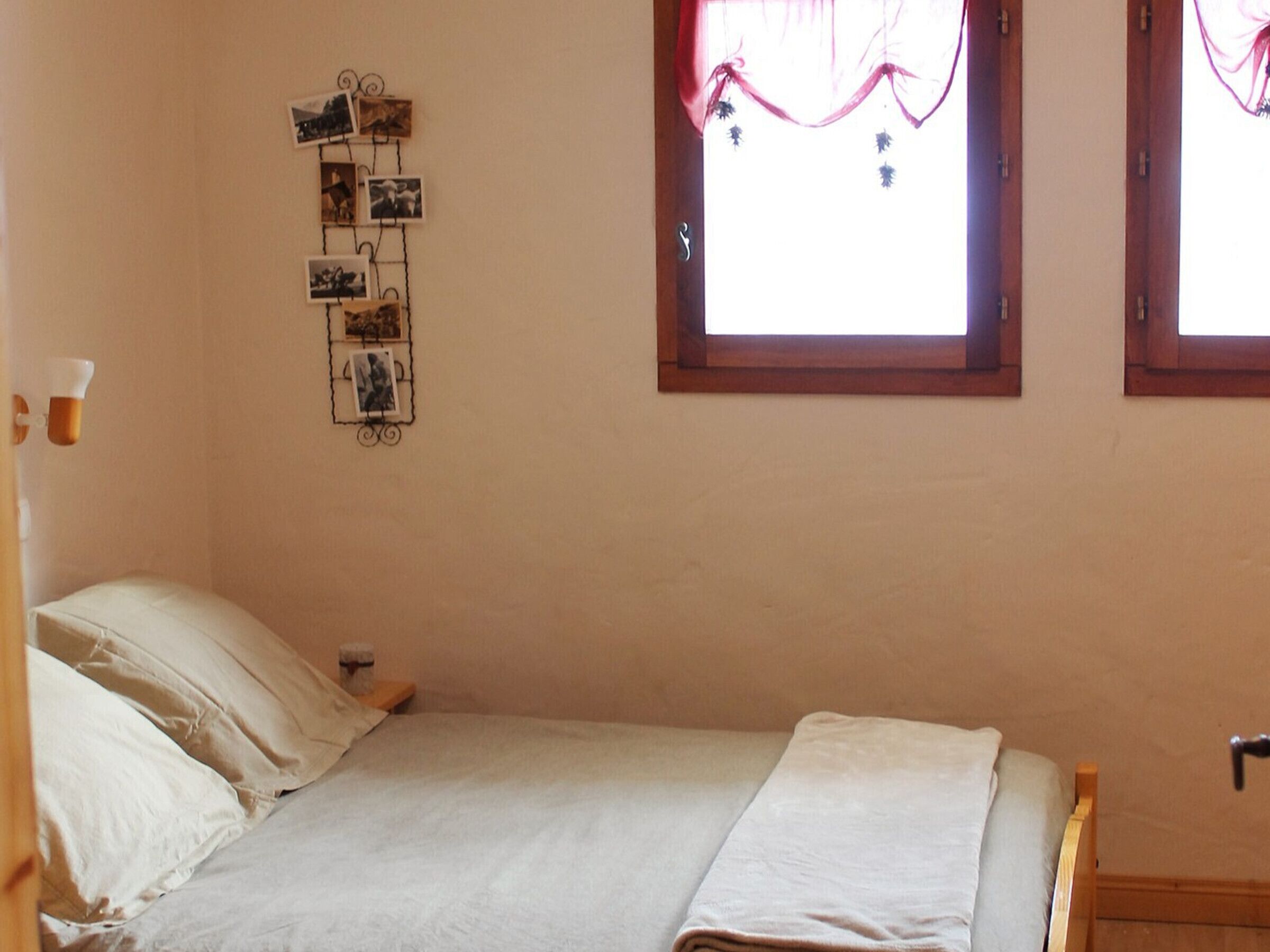 A bedroom with a bed, a wall-mounted photo collage, and two windows with curtains.