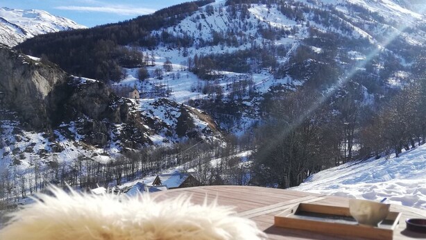 Um deck de madeira com vista para montanhas cobertas de neve e um pequeno edifício ao longe.