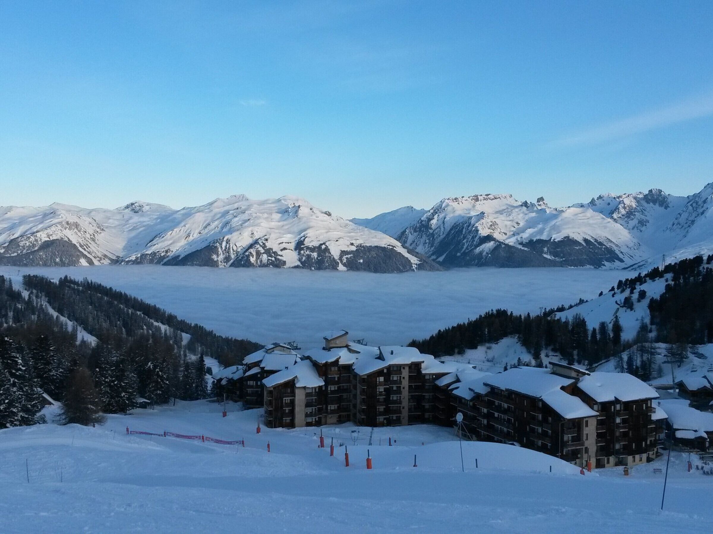 Estância de esqui alpina coberta por neve, com vários edifícios, pistas e vista panorâmica de picos nevados.