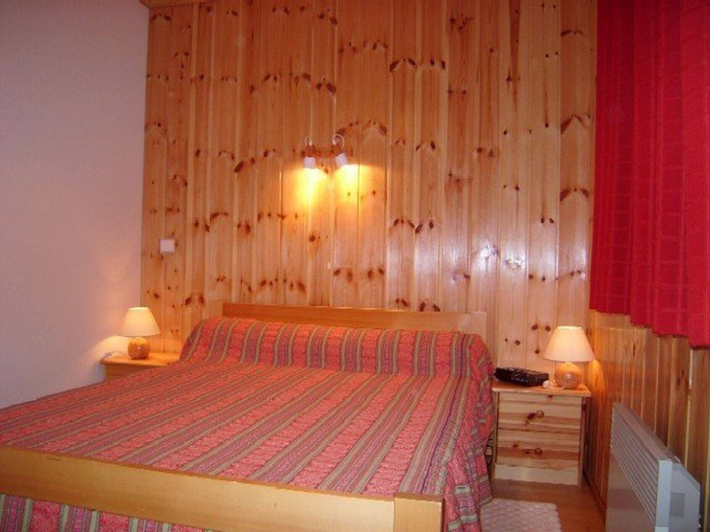A wooden-paneled bedroom with a bed, two bedside lamps, and a nightstand.
