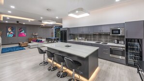 A modern kitchen with a central island, stainless steel appliances, and a dining area with bar stools. - 3BR Near Beach Tub & Pool Table V204 (Rawai)