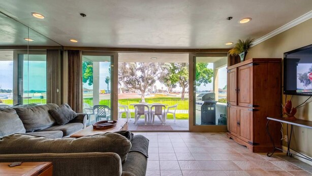 A modern living room with a sofa, a coffee table, and a TV mounted on the wall. There is a sliding glass door leading to an outdoor patio with a table and chairs. - Bayside Gem - Beachfront - Vibrant - Ocean Breeze (San Diego)