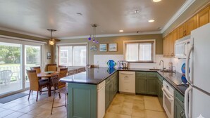 A kitchen with a central island, green cabinets, white appliances, and a dining area with chairs and a table. - Bayside Gem - Beachfront - Vibrant - Ocean Breeze (San Diego)