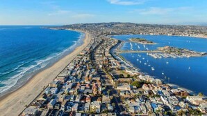 An aerial view of a coastal town with a long beachfront, a marina with boats, and dense residential buildings. - Bayside Gem - Beachfront - Vibrant - Ocean Breeze (San Diego)