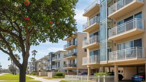 A multi-story residential building with balconies, a tree with red flowers, and a clear sky. - Bayside Gem - Beachfront - Vibrant - Ocean Breeze (San Diego)