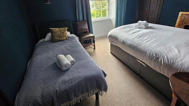 A bedroom with two beds, a window with curtains, a chair, and a door. - 2 Bed Apartment - Sleeps 4 - Parking - Wifi (Doncaster)