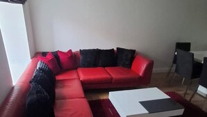 A red sectional sofa with black and red cushions, a white coffee table, and a red rug in a living room with wooden flooring. - 2 Bed Apartment - Sleeps 4 - Parking - Wifi (Doncaster)