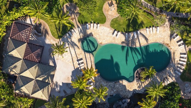 Luftaufnahme eines Resorts mit Schwimmbad, Liegebereichen und Palmen.