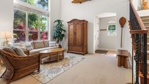 Ein geräumiges Wohnzimmer mit großem Fenster, einer Holzkommode, einem Rattansofa und einer Treppe.