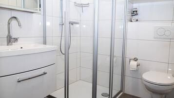 A modern bathroom with a glass-enclosed shower, a white sink, and a toilet.